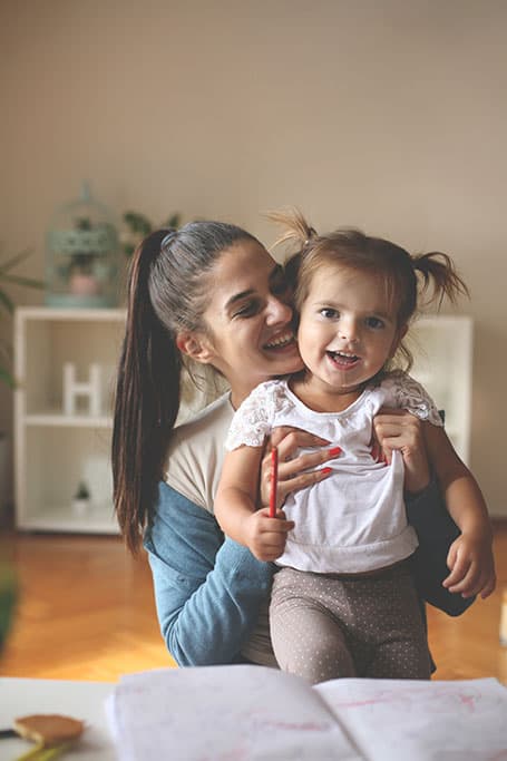 mujer sonriente cargando en brazos a una niña contenta