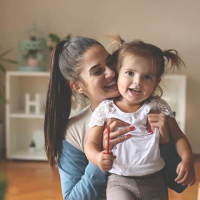 mujer sonriente cargando en brazos a una niña contenta